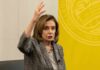 Nancy Pelosi gestures while speaking in front of yellow backdrop.