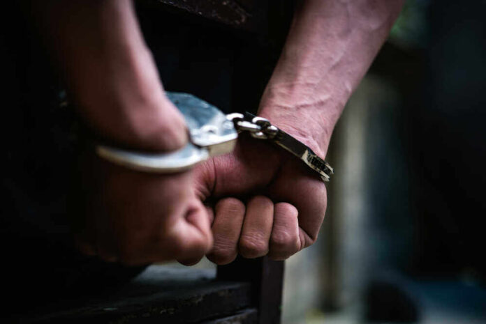 shutterstock_1338116366.jpg featured image Close-up of hands in handcuffs behind back.