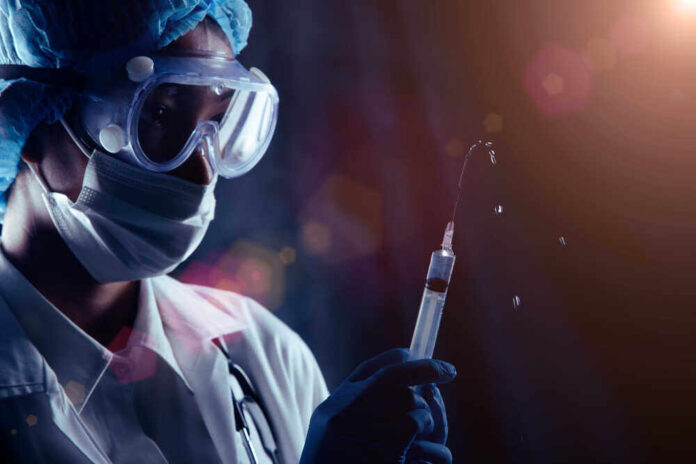 shutterstock_1880299123.jpg featured image Person in PPE holding syringe with liquid droplets.
