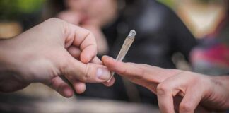 Hands passing a lit joint outdoors.