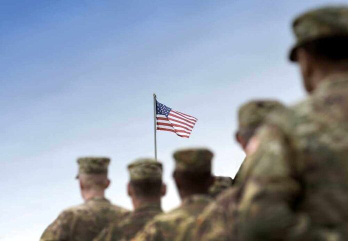 shutterstock_2380883205.jpg featured image Soldiers in uniform facing American flag outdoors.
