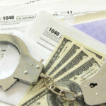 Handcuffs, dollar bills, and tax forms on a table.