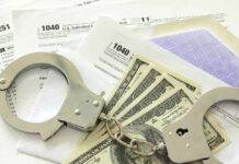 Handcuffs, dollar bills, and tax forms on a table.