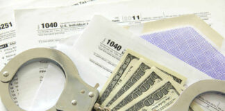 Handcuffs, dollar bills, and tax forms on a table.