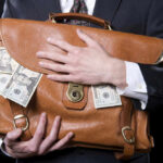 Person holding briefcase with money protruding from it