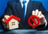 Businessman holding house model and prohibition sign