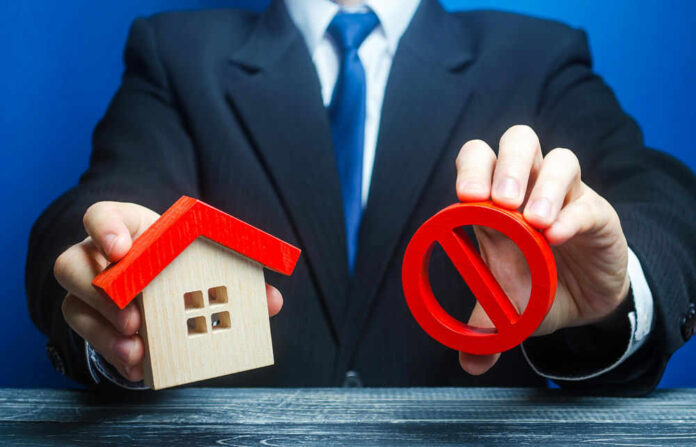 Businessman holding house model and prohibition sign