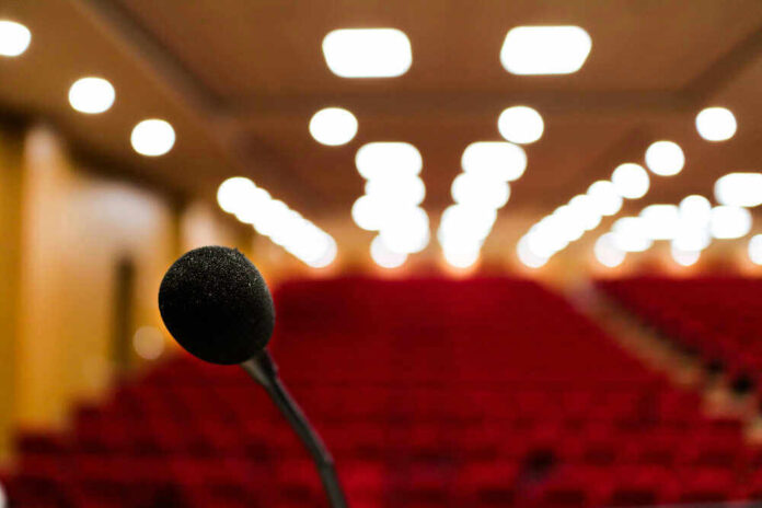 shutterstock_1823110904.jpg Microphone in focus, blurred audience seats and lights.