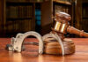 Wooden gavel and handcuffs on a table.