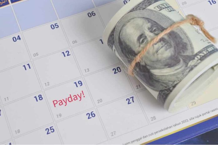 A rolled bundle of cash placed on a calendar marked with 'Payday!'