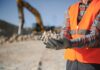 Construction worker holding rocks at a site with an excavator in the background