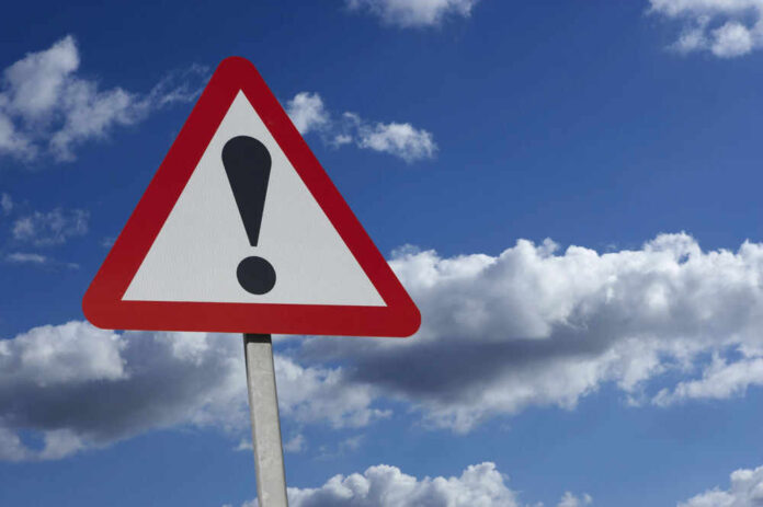 Warning sign with exclamation mark against sky