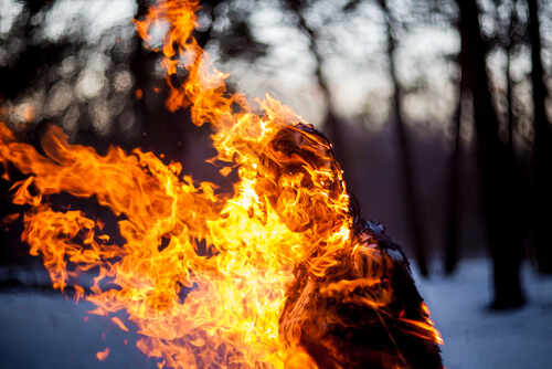 A silhouette of a person engulfed in flames in a forest setting