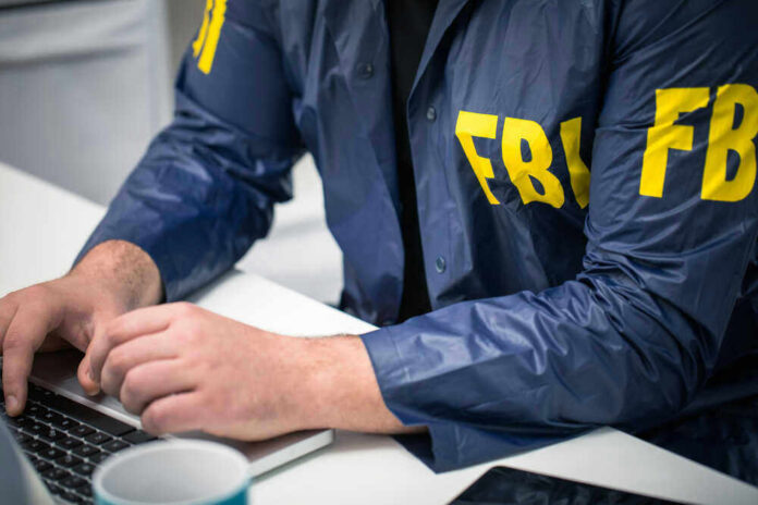 Person in FBI jacket working on laptop.