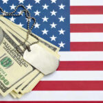 A stack of dollar bills on an American flag with a military dog tag
