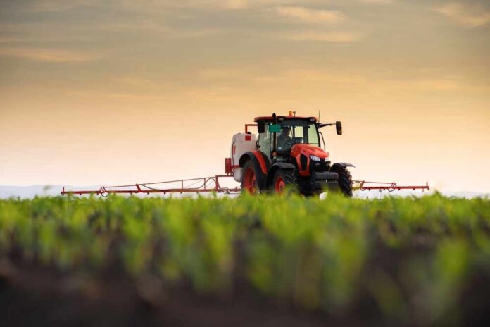 A tractor spraying crops in a field during sunset