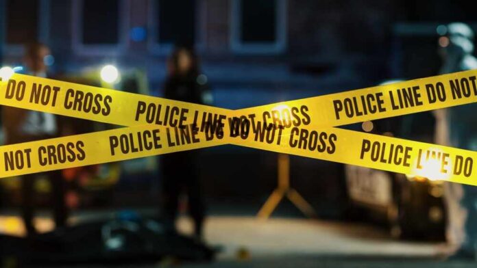 Police tape marking a crime scene with blurred figures in the background