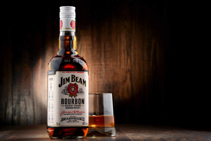 Bottle of Jim Beam bourbon next to a glass of whiskey on a wooden surface