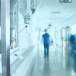 The Medical Crisis Nobody Saw Coming Hospital corridor with IV drip and healthcare worker.