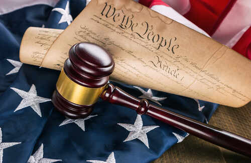 A gavel resting on an American flag with a scroll of the Constitution