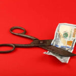 Scissors cutting a hundred dollar bill on a red background