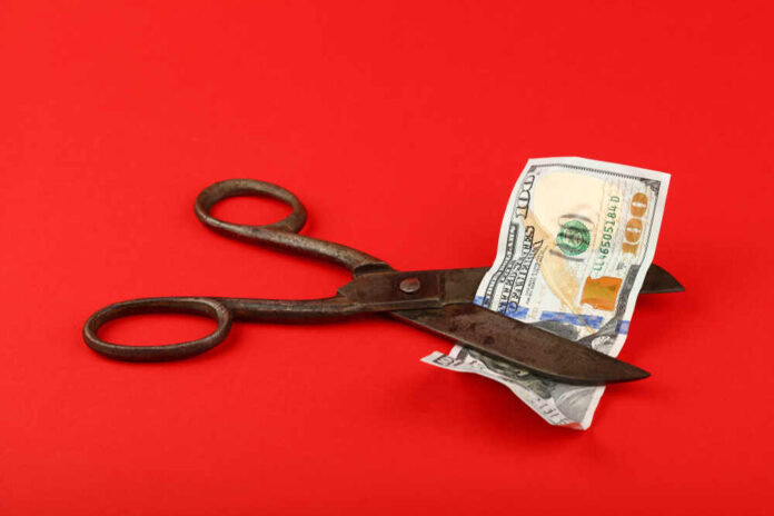 Scissors cutting a hundred dollar bill on a red background