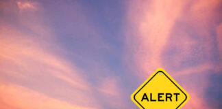 Yellow alert sign against a colorful sunset sky