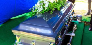 A silver casket adorned with flowers at a gravesite