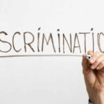 A hand writing the word 'DISCRIMINATION' on a white background