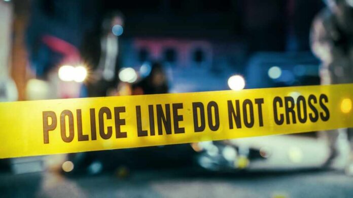 Police line caution tape at a crime scene with blurred figures in the background