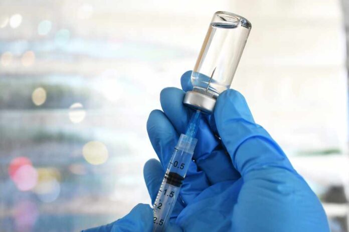 A gloved hand holding a syringe and a vial of liquid