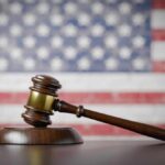 Judge BLOCKS Trump Report Hours Before Release A wooden gavel resting on a sound block with an American flag background