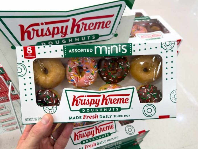 A hand holding a box of assorted mini Krispy Kreme doughnuts