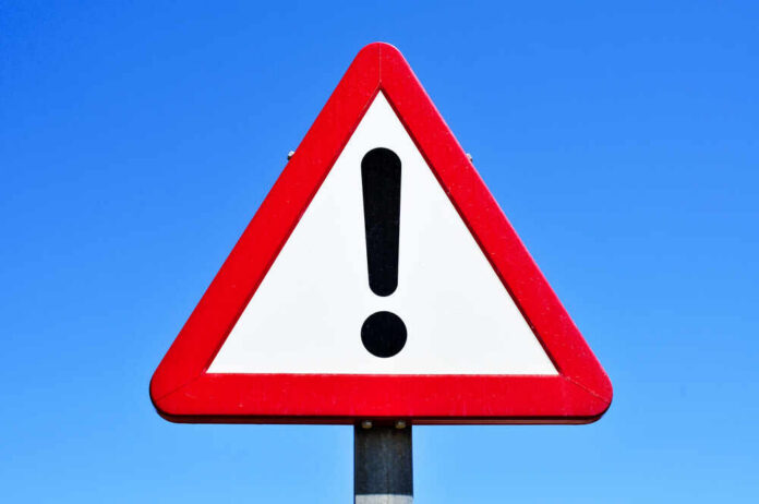 A triangular warning sign with an exclamation mark against a blue sky