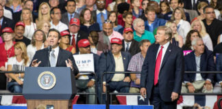 A man speaks at a podium as another man watches.