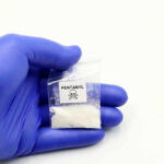 DEADLY Fentanyl Found Hidden in Barbie Doll Hand in glove holding fentanyl packet with skull warning.