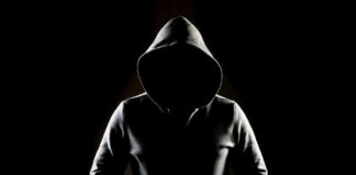 Hooded figure in darkness with hidden face.