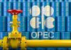 Yellow pipeline valve in front of blue oil barrels with OPEC logo