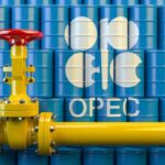 Yellow pipeline valve in front of blue oil barrels with OPEC logo