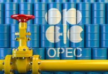 Yellow pipeline valve in front of blue oil barrels with OPEC logo