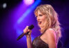 Taylor Swift performing with microphone on stage, colorful lighting.