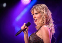 Taylor Swift performing with microphone on stage, colorful lighting.
