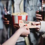 Hands exchanging a cinema ticket with popcorn in the background