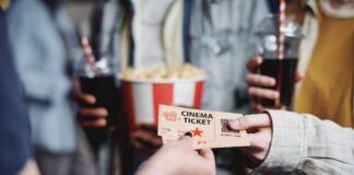 Hands exchanging a cinema ticket with popcorn in the background