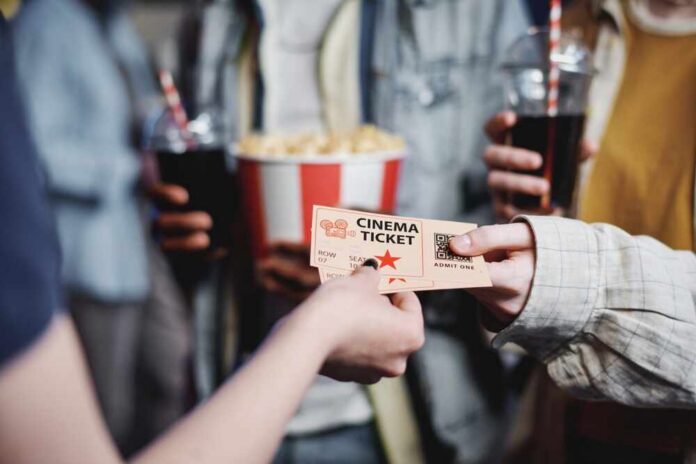 Hands exchanging a cinema ticket with popcorn in the background