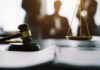 Gavel and scales in courtroom with blurred figures behind.
