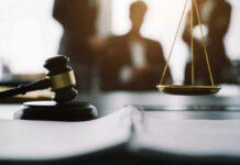 Gavel and scales in courtroom with blurred figures behind.