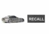 RECALL Hits 422,000 Fords A miniature gray sports car next to a black sign that reads 'RECALL'