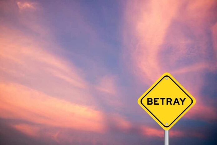 shutterstock_2407896513.jpg A yellow warning sign with the word 'BETRAY' against a colorful sunset sky