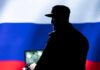 Silhouette of a military personnel in front of the Russian flag using a laptop